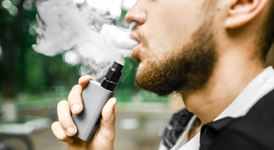 Person vaping outdoors, exhaling vapor.