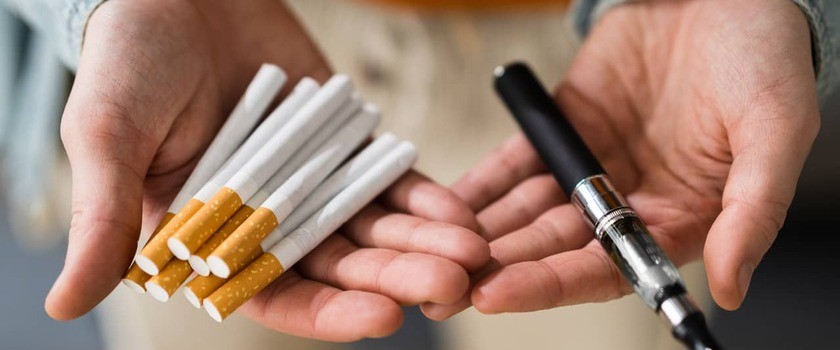 Hands holding traditional cigarettes and a vape pen.