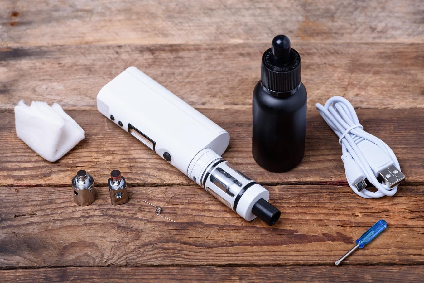 Vaping kit with e-liquid and accessories on wood.
