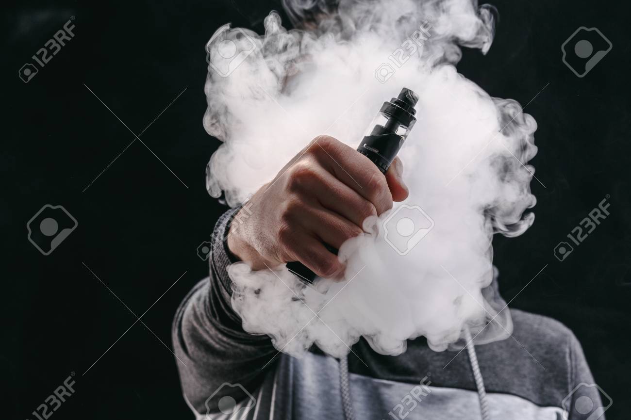 Zdjęcie osoby trzymającej i używającej e-papierosa, z widoczną chmurą pary.