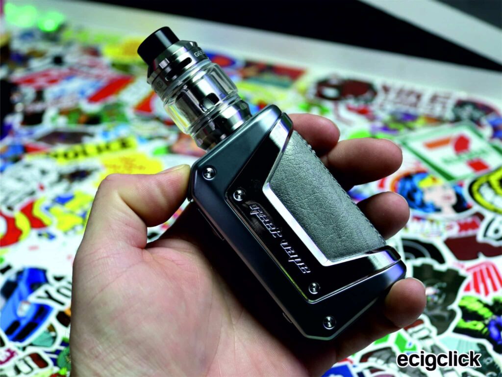Hand holding a sleek vape device against stickers.