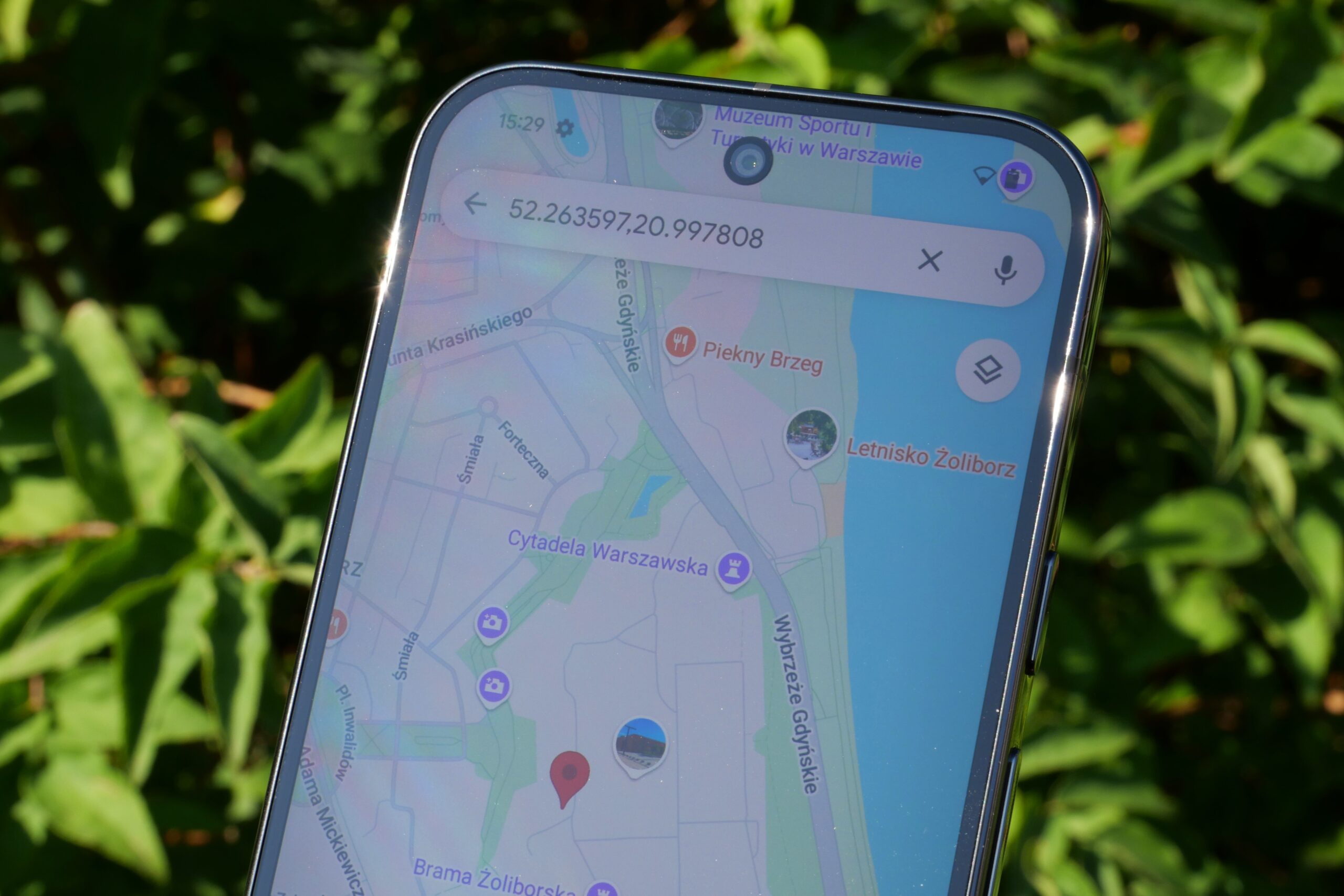 Ręka trzymająca smartfon z otwartą aplikacją Google Maps, obok leży uszkodzony e-papieros