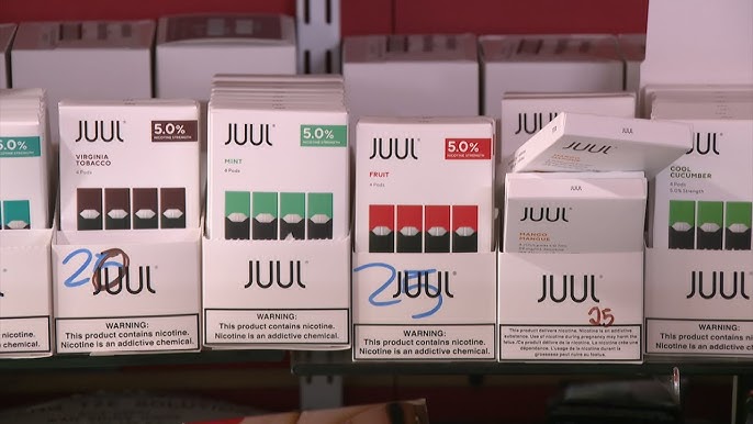 Sprzedawca w sklepie z e-papierosami, siedzący za ladą i beznamiętnie patrzący w telefon, ignorujący klienta.