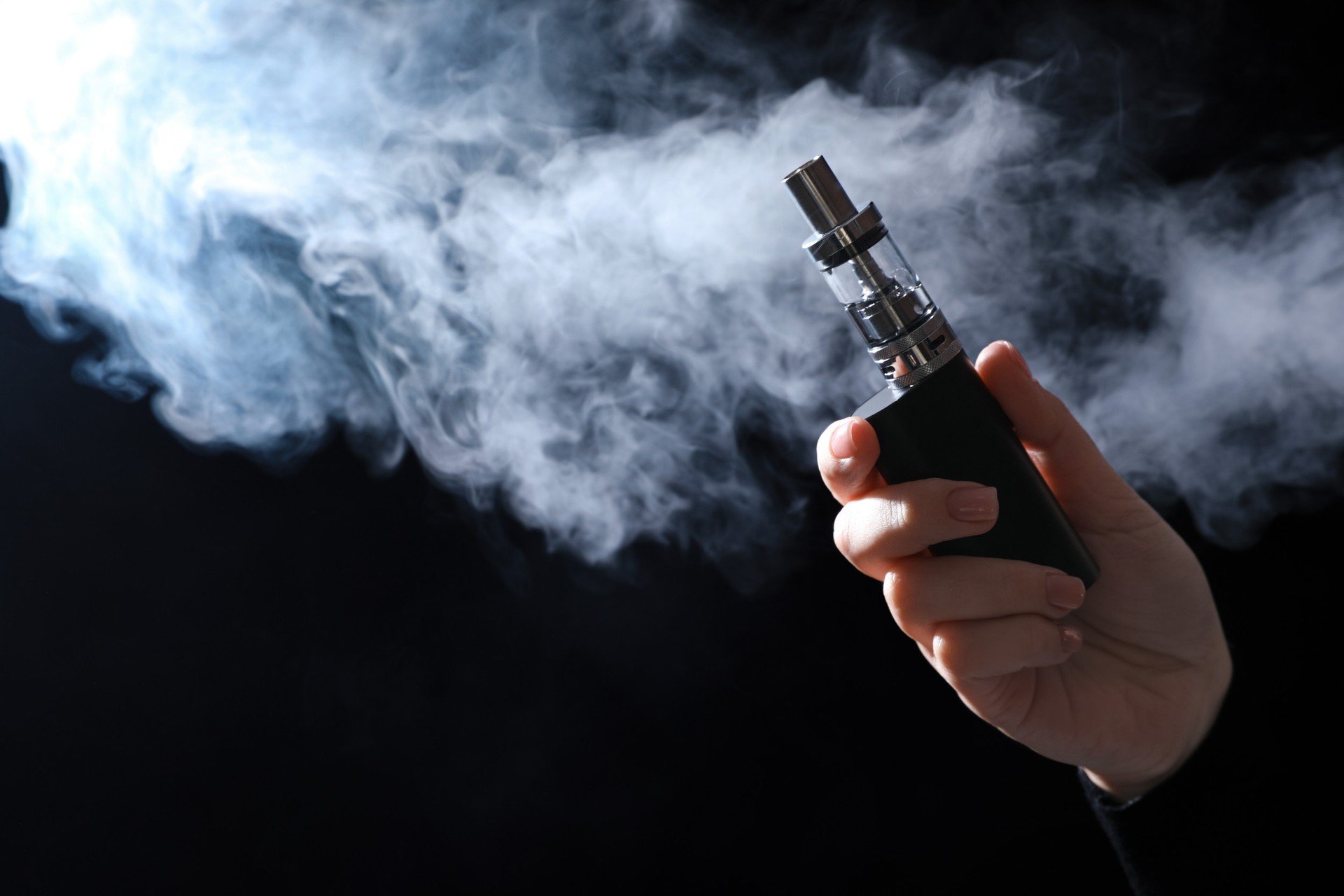 Profesjonalnie wyglądający mężczyzna w garniturze (doradca finansowy) wskazujący na wykresy i e-papierosy, symbolizujący doradztwo w kwestii vapingu.