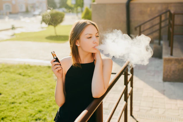 kobieta kupuje oczami e-papieros, modna dziewczyna z estetycznym vape, stylizowany e-papieros paznokcie - Urocza modna dziewczyna pali e-papierosa vaping podczas spaceru po ...